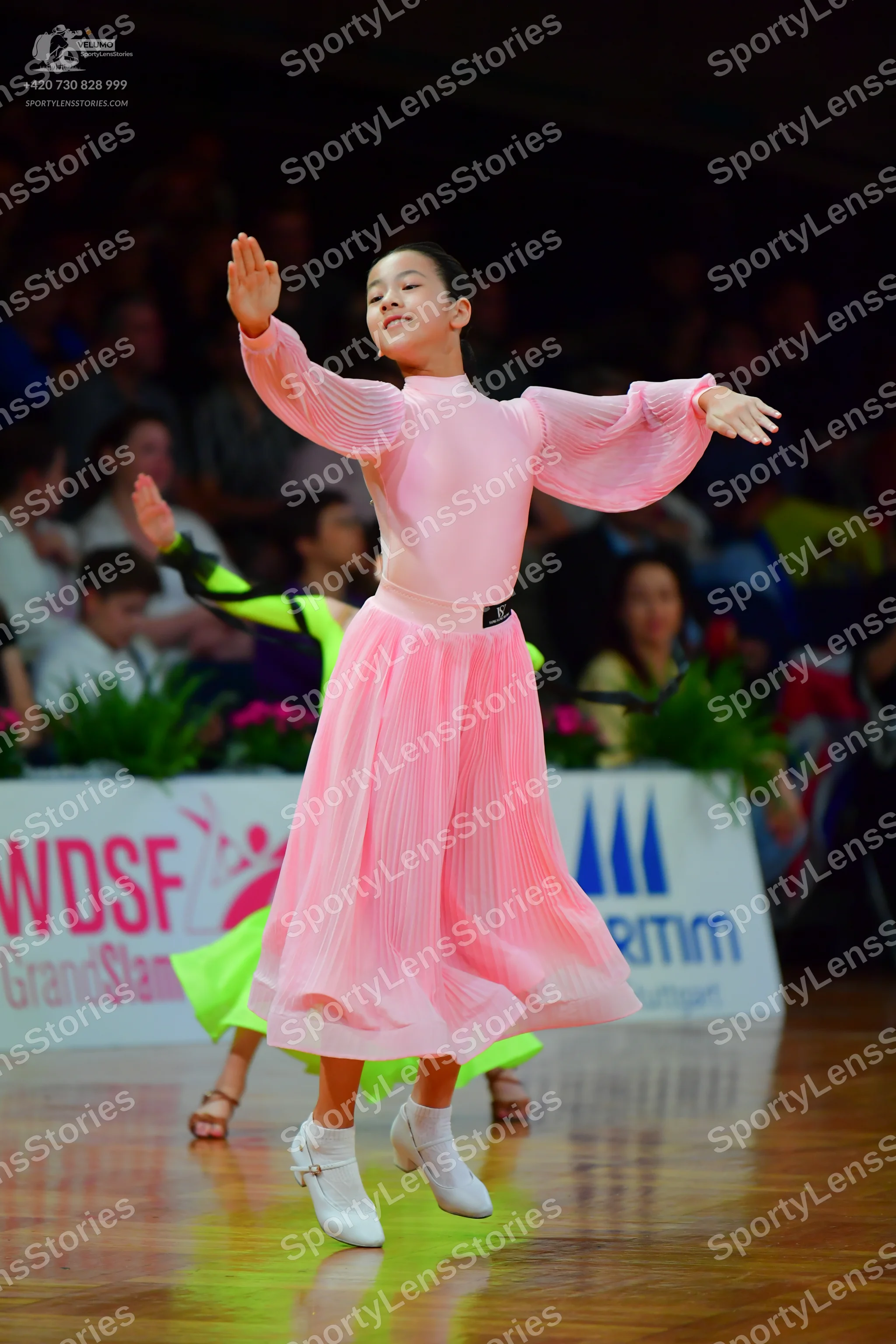 Dancesport competitor: Female dancer in foreground: light pink long-sleeved ballroom dress with a pleat