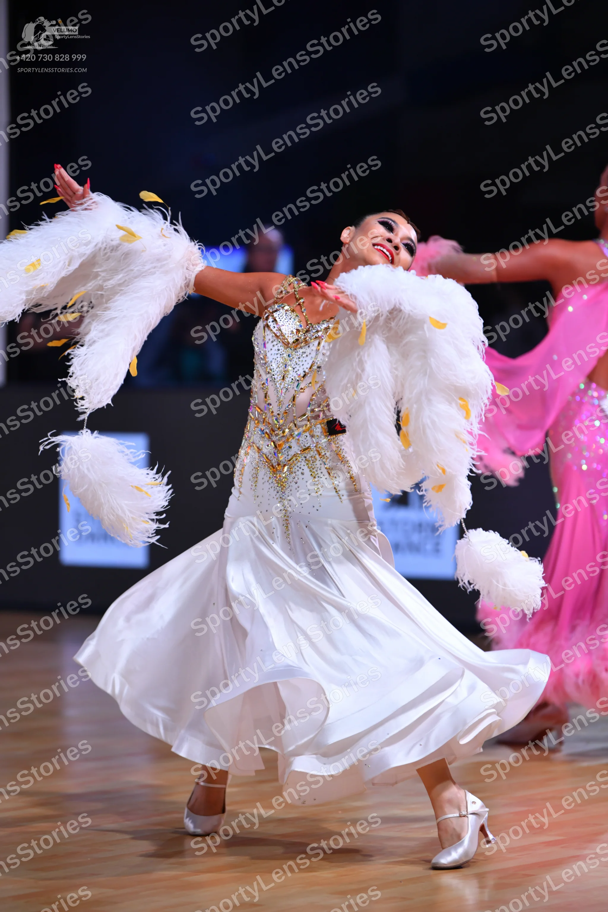 Dancesport competitor: Female dancer 1: white ballroom gown with a gold-sequined bodice and large white