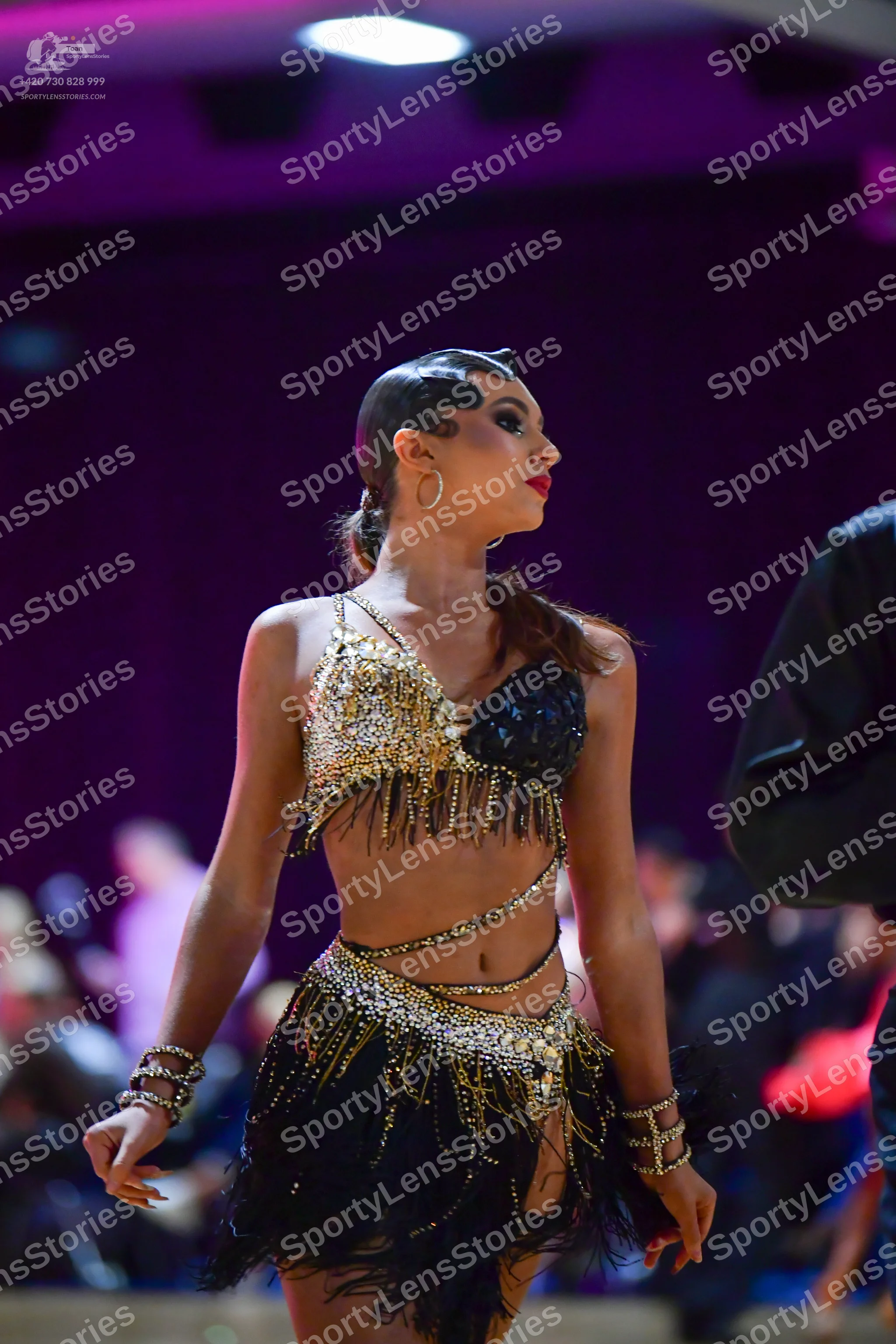 Dancesport competitor: Female dancer: gold and black Latin dance costume featuring a sequined crop top