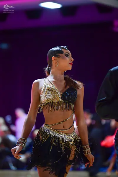 Dancesport competitor: Female dancer: gold and black Latin dance costume featuring a sequined crop top 