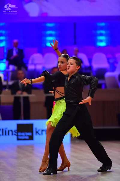 Dancesport competitor: Female dancer: black long-sleeved crop top and lime green fringe skirt