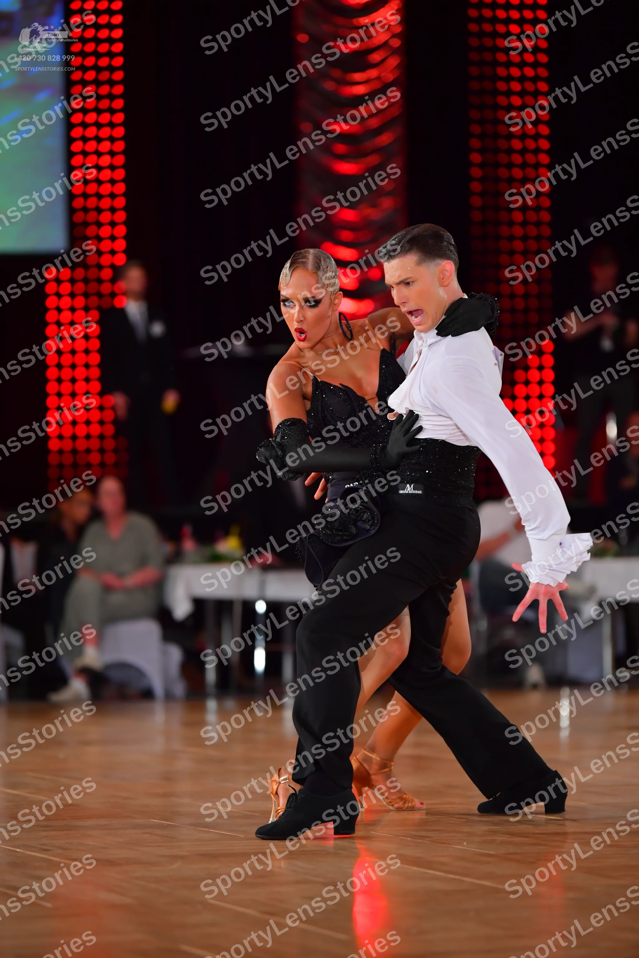 Dancesport competitor: Male dancer: white long-sleeve shirt with ruffled cuffs, black trousers, and a b