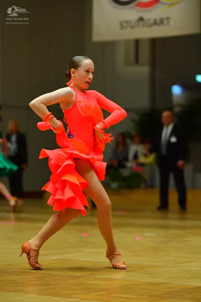 Dancesport competitor: Female dancer: bright orange latin dress with a multi-layered ruffled skirt and 