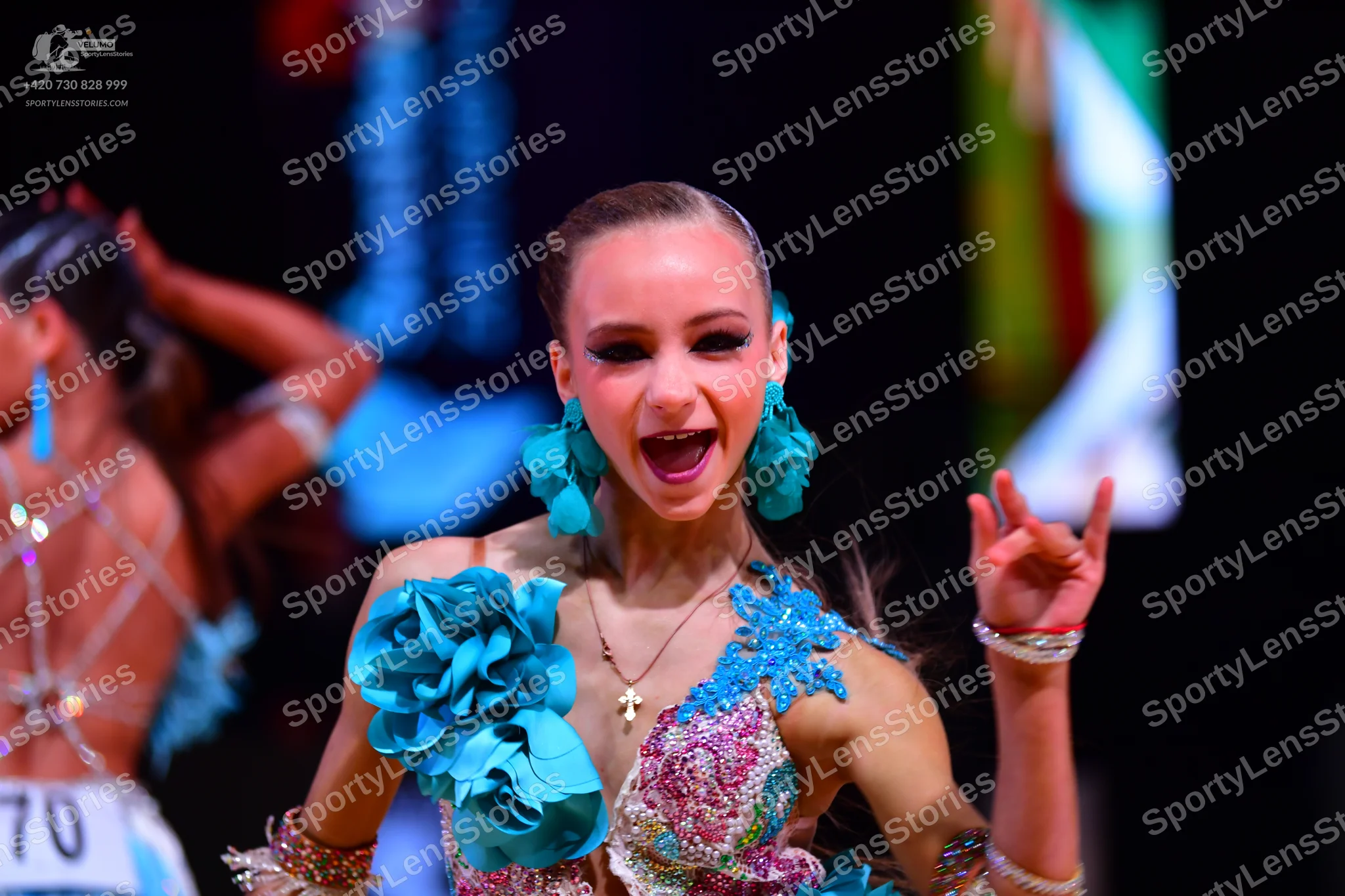 Dancesport competitor: Female dancer in foreground: blue and pink latin dance dress with heavy sequin a
