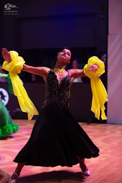 Dancesport competitor: Female dancer: black ballgown with a gold sequined bodice and long, flowing yell