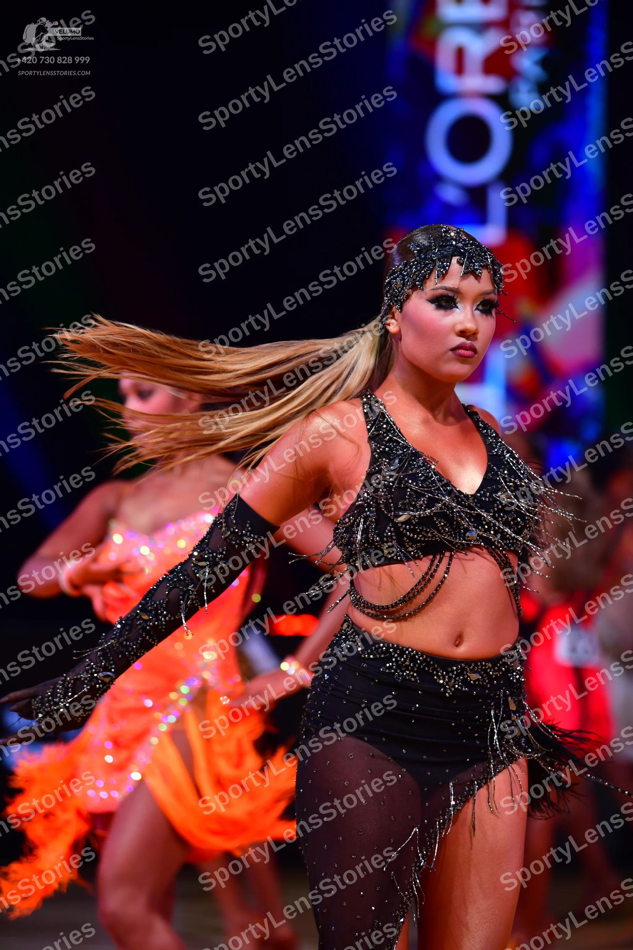 Dancesport competitor: Female dancer in foreground: black latin dance costume featuring a sequined crop