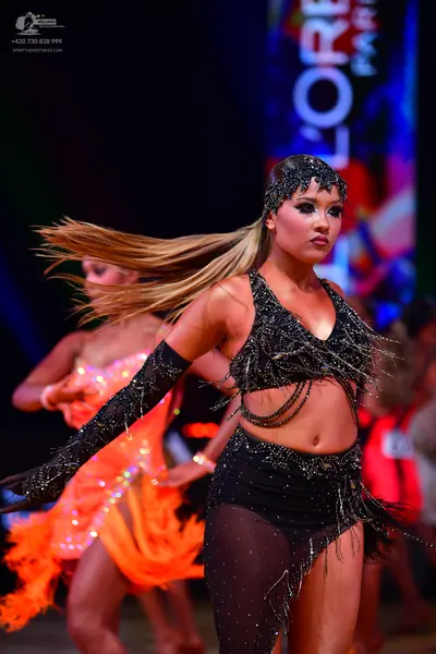 Dancesport competitor: Female dancer in foreground: black latin dance costume featuring a sequined crop