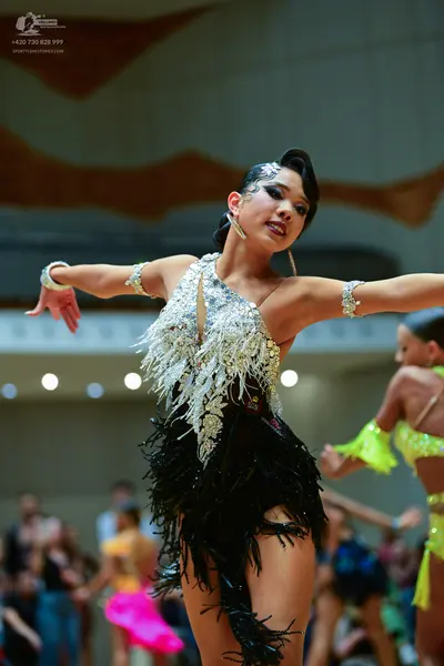 Dancesport competitor: Female dancer in foreground: silver and white sequined top with metallic fringe 