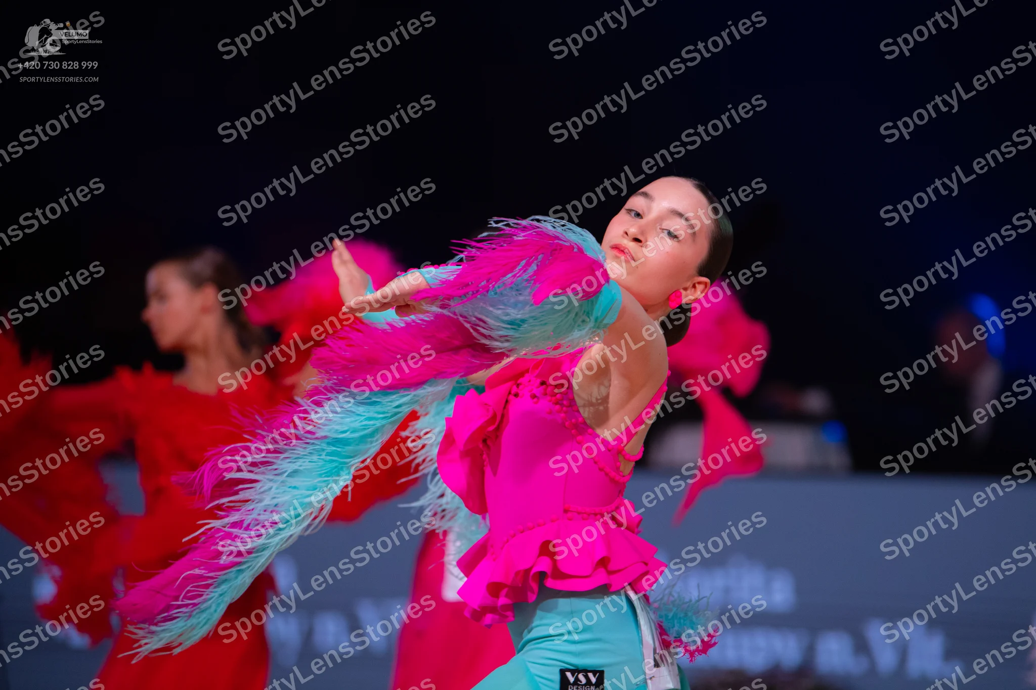 Dancesport competitor: Female dancer in foreground: bright pink latin dress with light blue fringe and