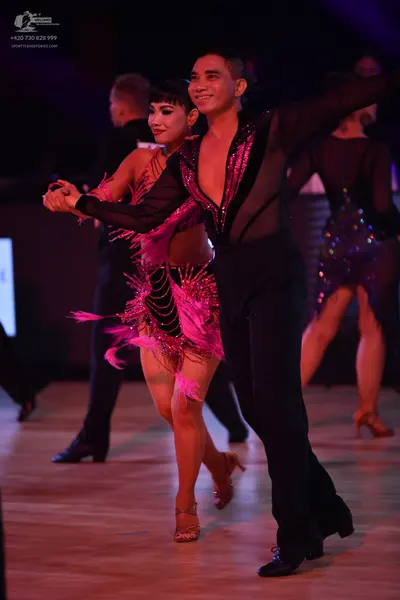 Dancesport competitor: Female dancer in foreground: magenta latin dress with sequins and long fringe
