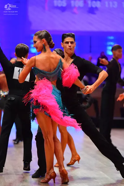 Dancesport competitor: Female dancer: teal sequined Latin dress with bright pink feather fringe and tea