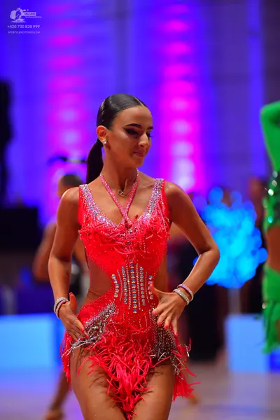 Dancesport competitor: Female dancer in foreground: red Latin dress with sequins, cutouts, and fringe, 