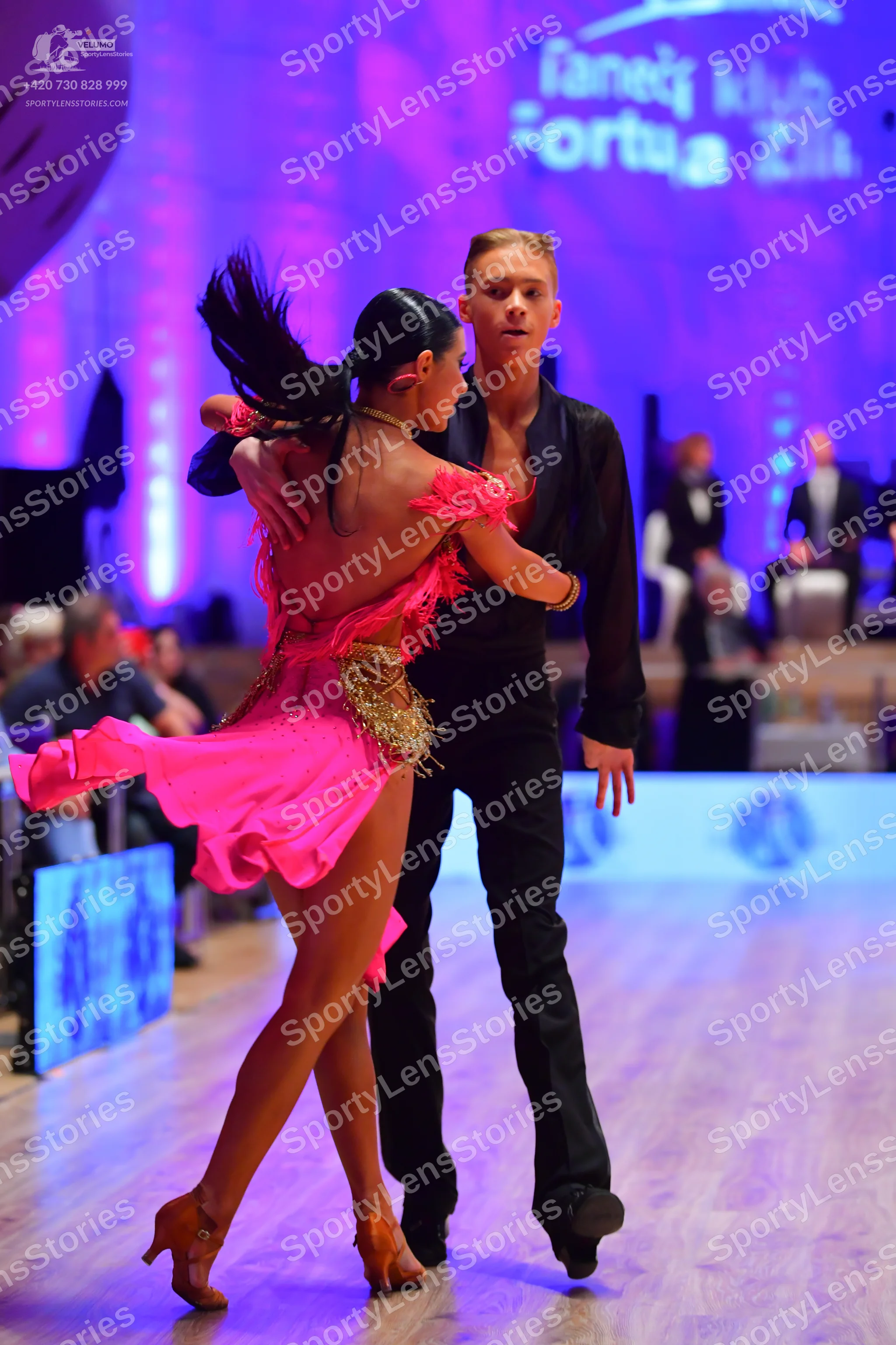 Dancesport competitor: Female dancer: bright pink Latin dance dress with feather-like fringe on the bac