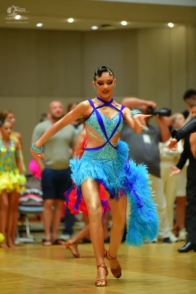 Dancesport competitor: Female dancer in foreground: light blue Latin dress with sequins, mesh panels, a