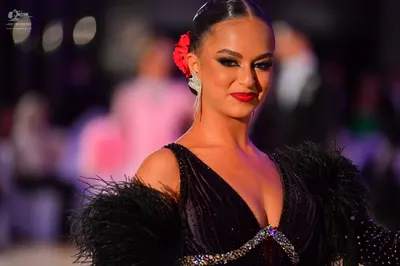 Dancesport competitor: Female dancer: black Latin dress with large black feathers on the shoulders, dec