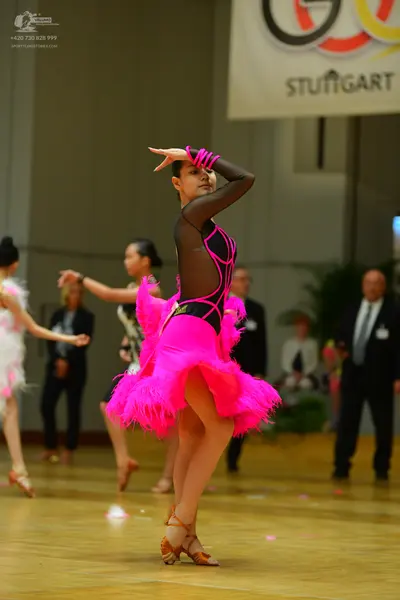 Dancesport competitor: Female dancer in foreground: black long-sleeved latin dress with pink trim and a