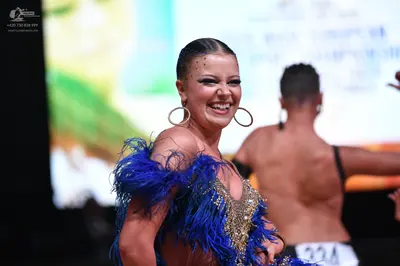 Dancesport competitor: Female dancer: blue and gold latin dress with blue feathers and gold sequins