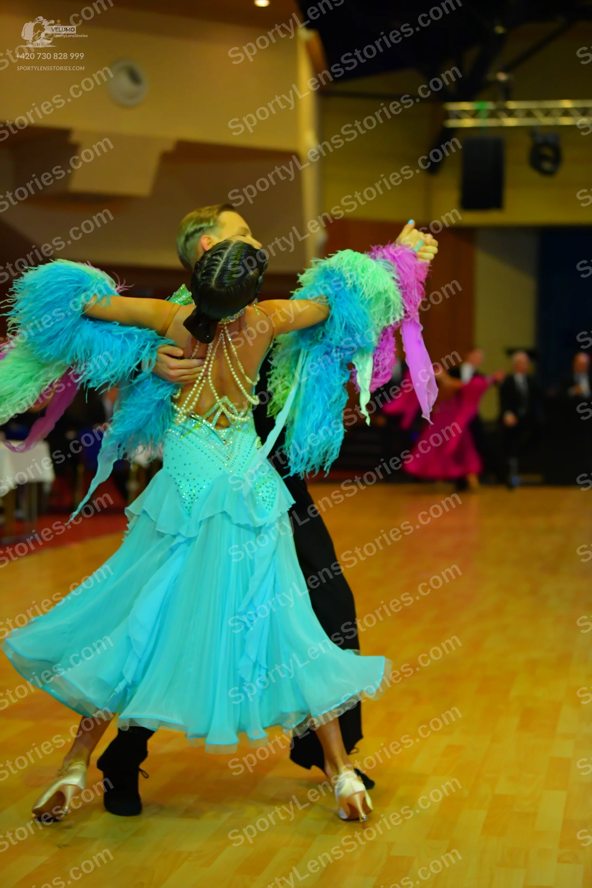 Dancesport competitor: Female dancer in foreground: light blue ballgown with beaded strands and large c