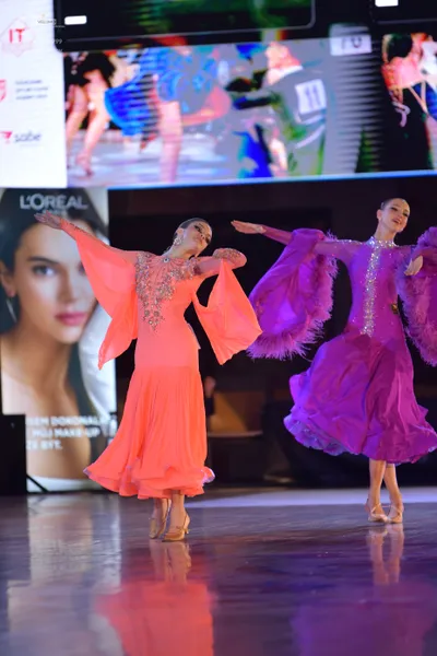 Dancesport competitor: Female dancer 1: coral-colored ballroom dress with long flared sleeves and a seq