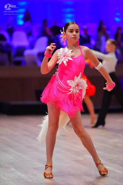 Dancesport competitor: Female dancer: bright pink Latin dance dress with fringe, large white 3D flower 