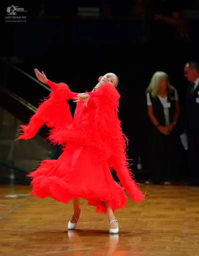 Dancesport competitor: Female dancer: red latin dress with long fringe on the sleeves and skirt, white 