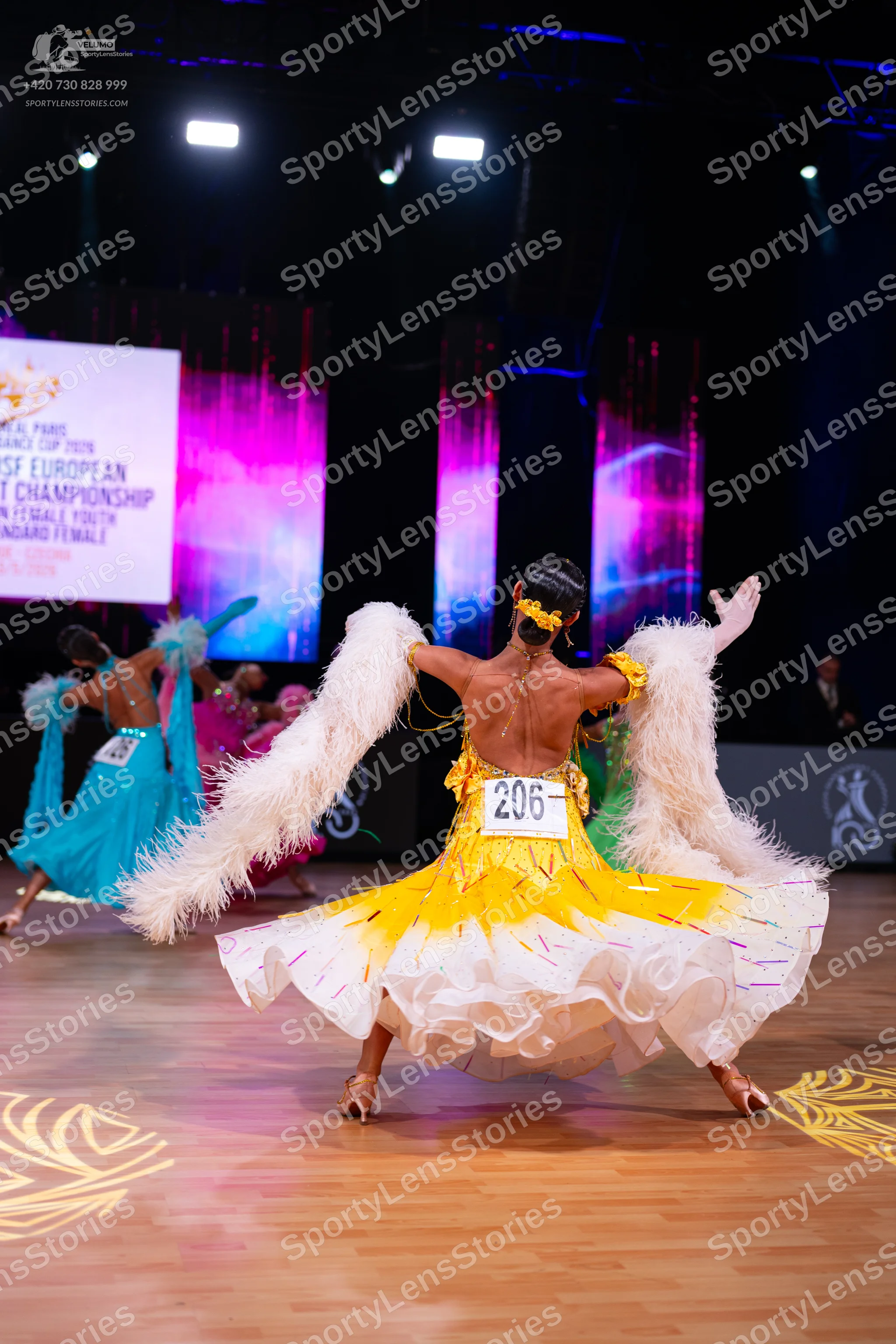 Dancesport competitor: Female dancer: white and yellow Latin dress with a flowing, multi-layered skirt