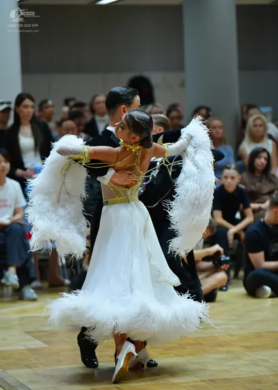 Dancesport competitor: Female dancer: white ballgown with a gold sequined bodice and large white feathe