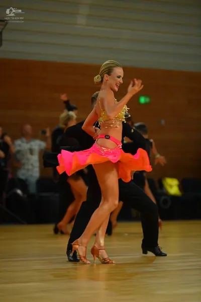 Dancesport competitor: Female dancer: bright orange/pink two-piece Latin costume with a gold/yellow seq
