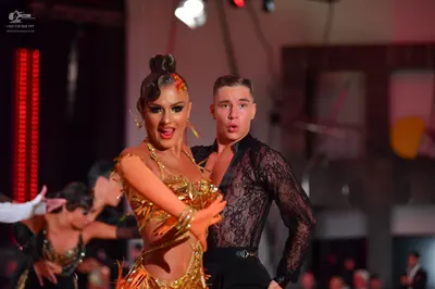 Dancesport competitor: Female dancer: gold/bronze latin dance costume with sequins and cutouts, and lar