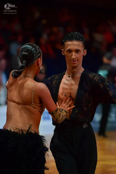 Dancesport competitor: Male dancer: black lace sheer shirt with long sleeves, black pants, and a thin s