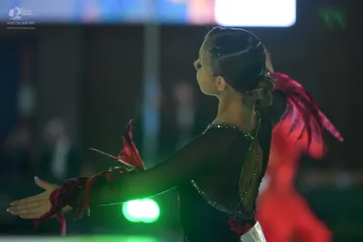 Dancesport competitor: Foreground dancer: black Latin dance costume with sheer sleeves, silver rhinesto