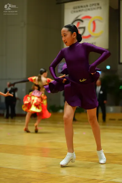 Dancesport competitor: Female dancer in foreground: dark purple long-sleeved dress with a high neckline