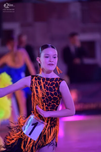 Dancesport competitor: Female dancer in foreground: black latin dress with orange honeycomb pattern and