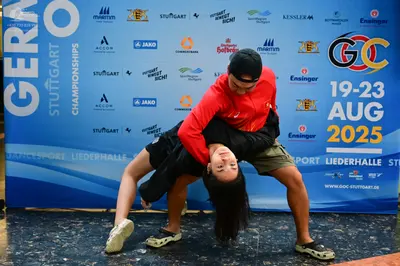 Dancesport competitor: Male dancer: red long-sleeved shirt, dark shorts, black baseball cap, and dark a
