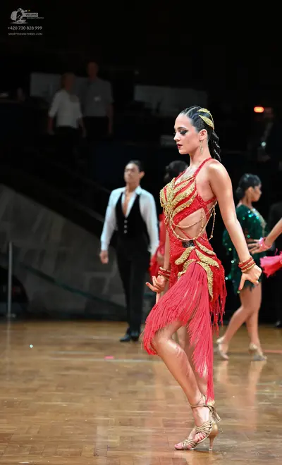 Dancesport competitor: Female dancer in foreground: red Latin dress with gold fringe and gold chain-lik