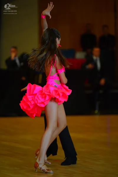 Dancesport competitor: Female dancer: neon pink Latin dance dress with a voluminous, multi-layered ruff