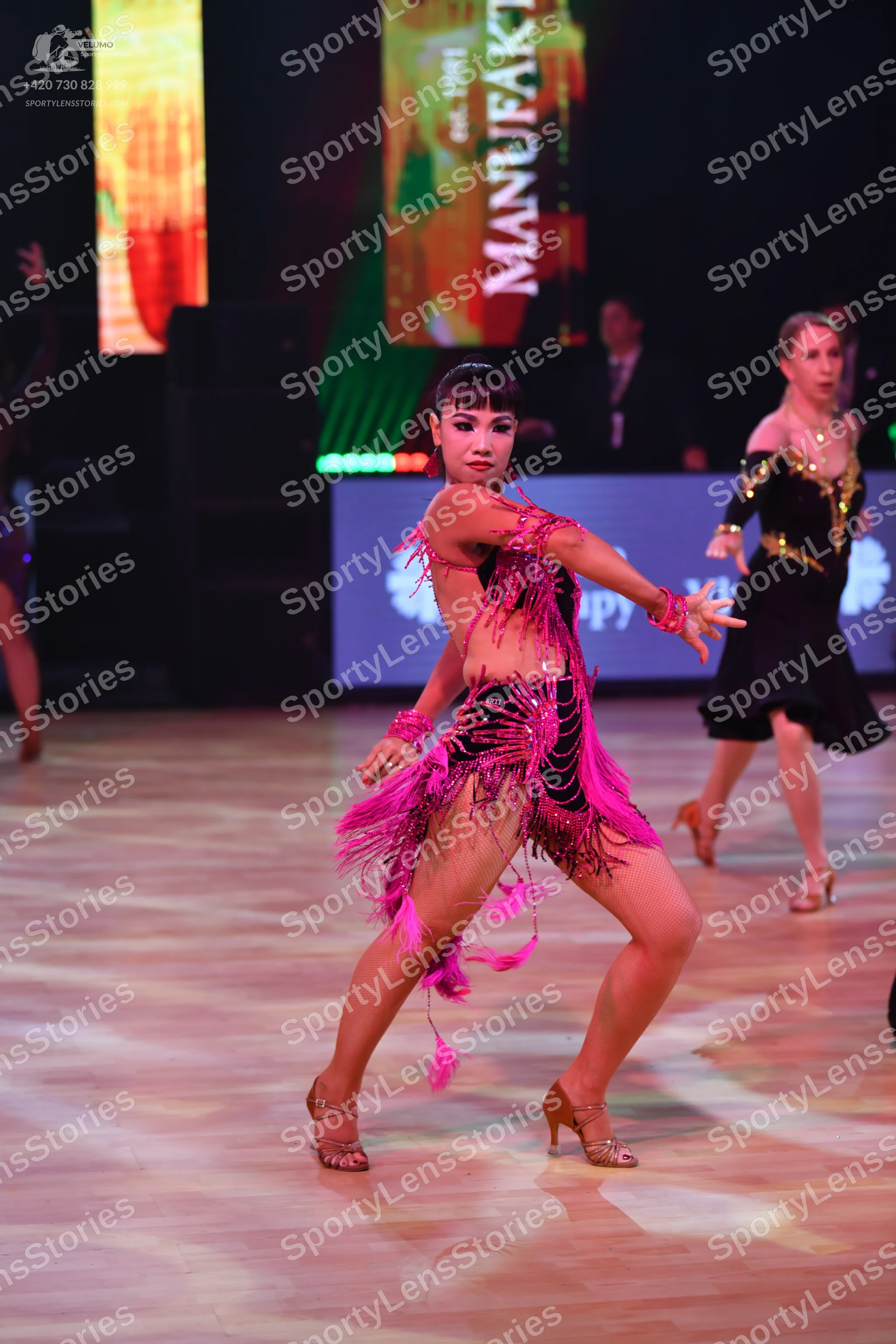 Dancesport competitor: Female dancer in foreground: bright pink Latin dance dress with fringe and cut-o
