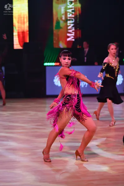 Dancesport competitor: Female dancer in foreground: bright pink Latin dance dress with fringe and cut-o