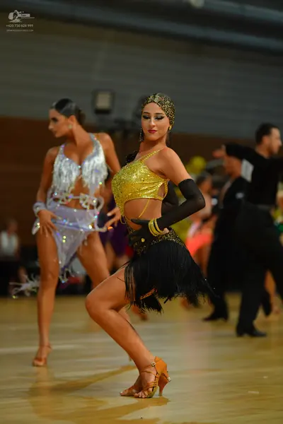 Dancesport competitor: Female dancer in foreground: gold sequin halter top and black fringe skirt with 