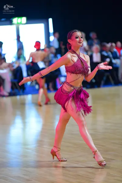 Dancesport competitor: Female dancer in foreground: magenta Latin dance costume with a sequin-covered h