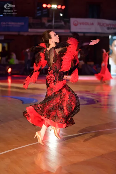 Dancesport competitor: Female dancer (foreground): red Latin dress with black lace overlay and long red
