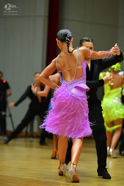Dancesport competitor: Female dancer in foreground: purple latin dress with fringe and shimmering detai