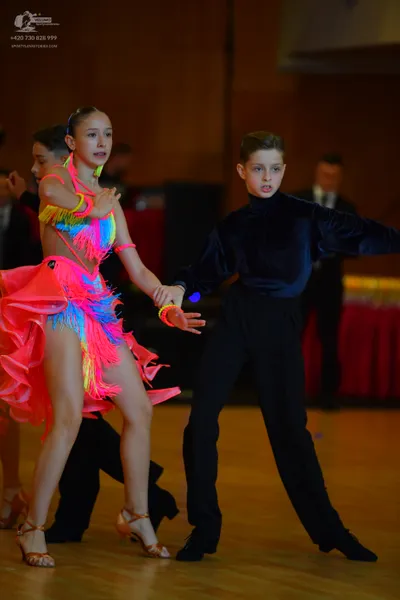 Dancesport competitor: Female dancer: bright pink, yellow, and blue Latin dance dress with fringe and m