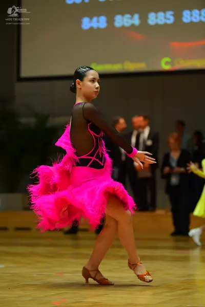Dancesport competitor: Female dancer: bright pink Latin dance dress with a black bodice featuring sheer