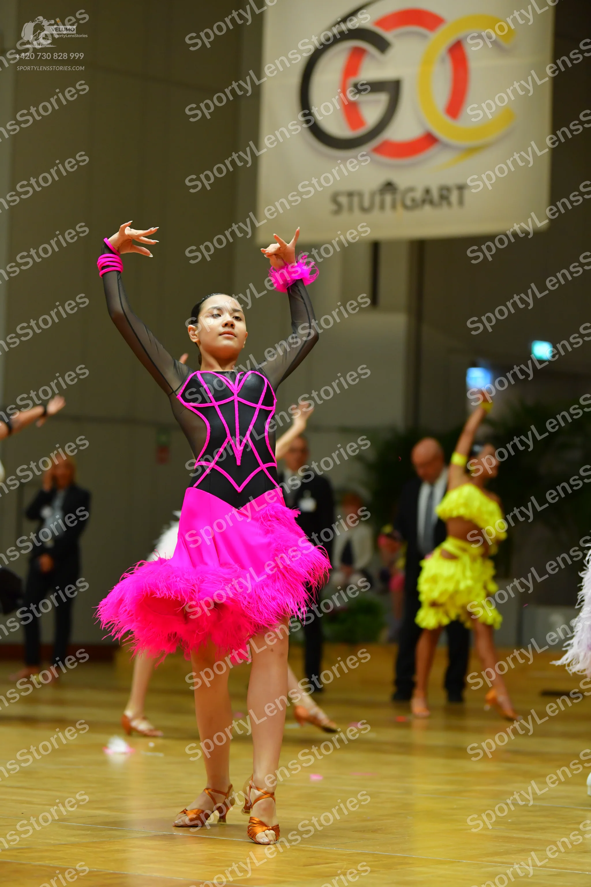Dancesport competitor: Female dancer in foreground: black Latin dance dress with pink decorative lines