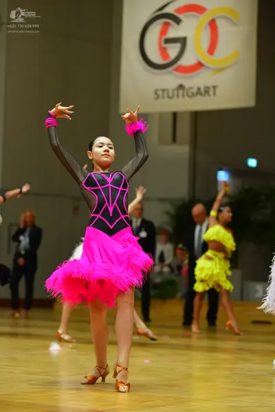 Dancesport competitor: Female dancer in foreground: black Latin dance dress with pink decorative lines 