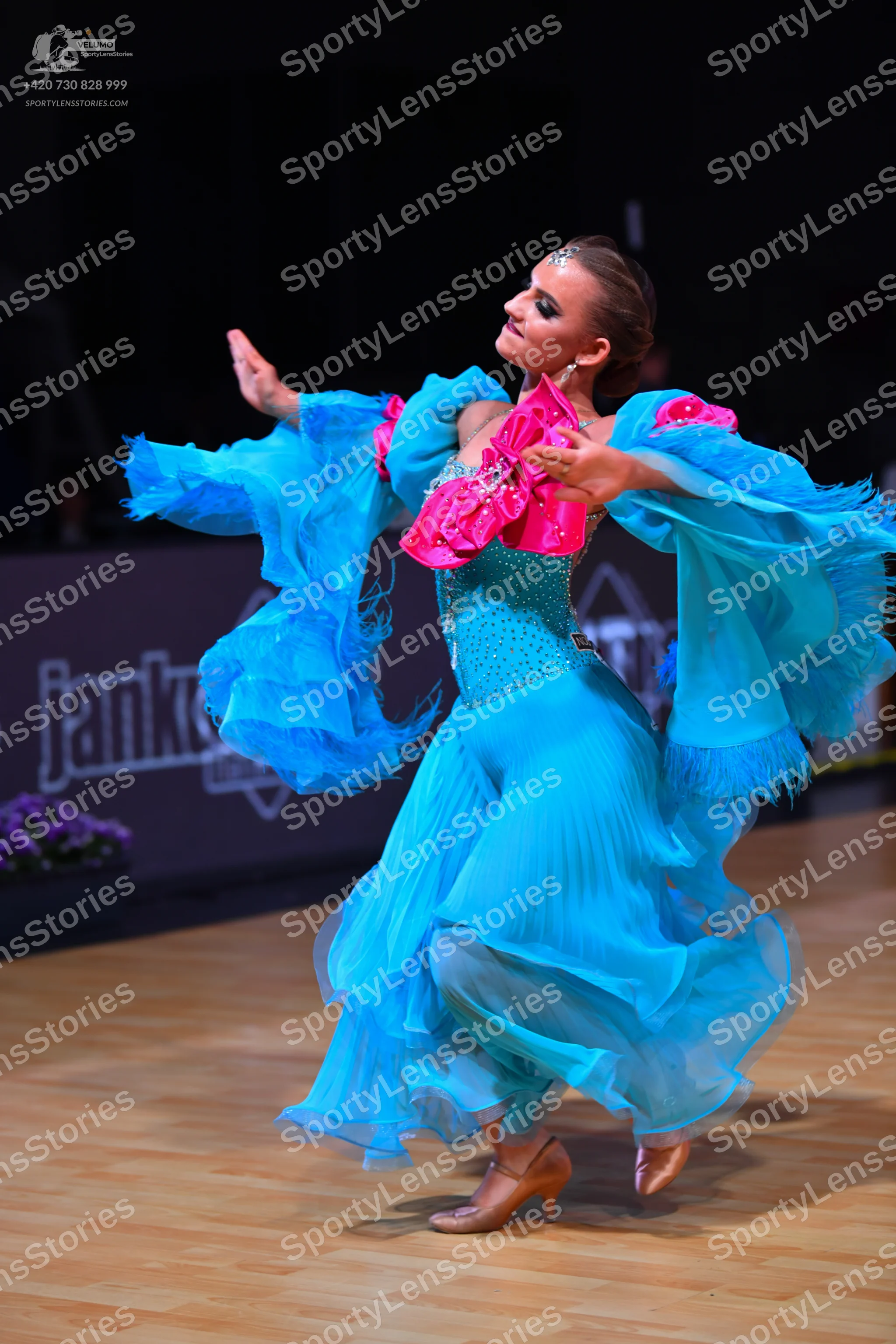 Dancesport competitor: Female dancer: bright blue ballroom dress with large, flowing, ruffled sleeves a