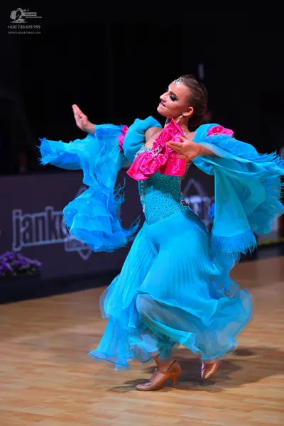 Dancesport competitor: Female dancer: bright blue ballroom dress with large, flowing, ruffled sleeves a