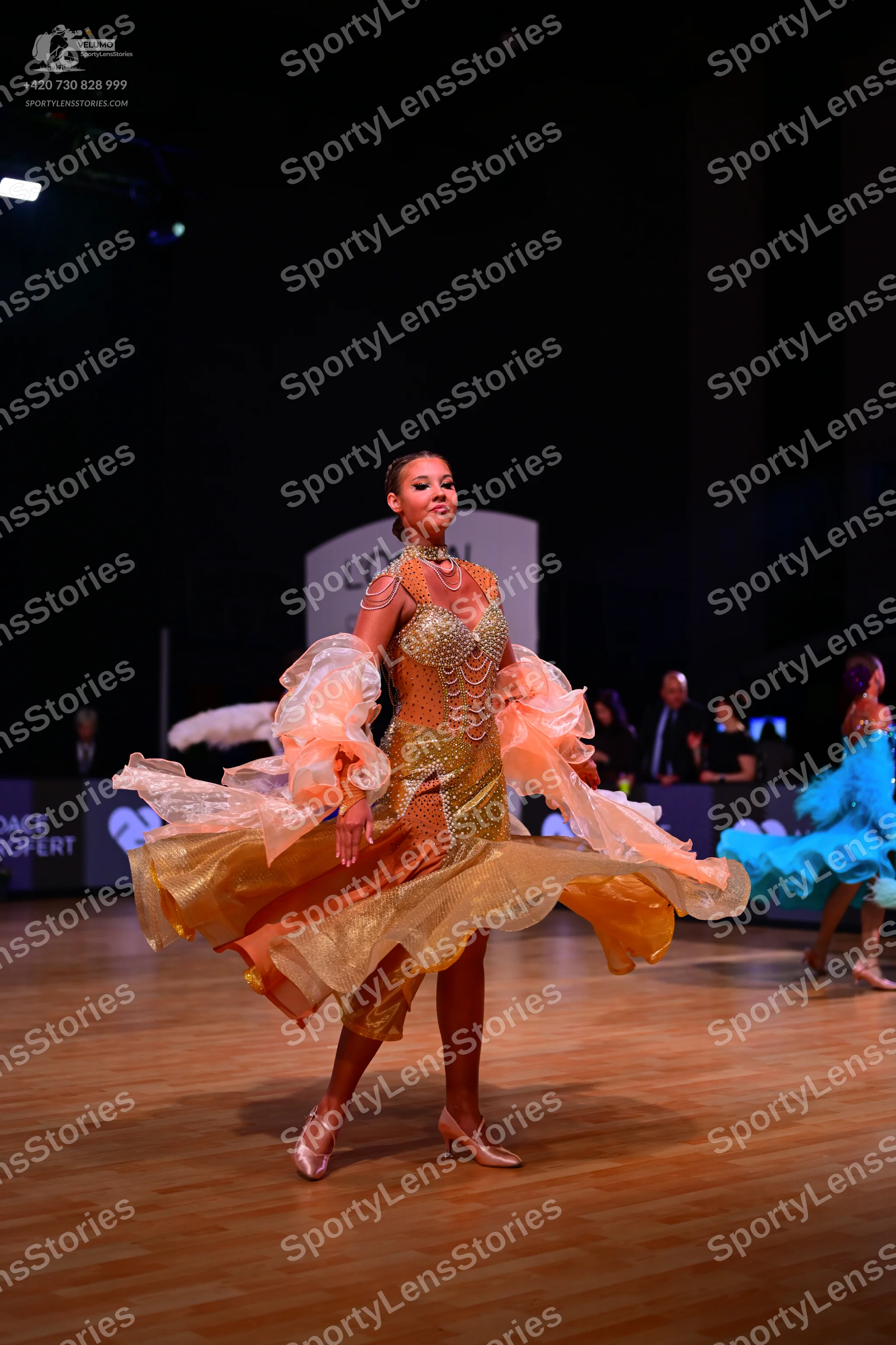 Dancesport competitor: Female dancer 1: gold ballroom dress with a sequined bodice and large, flowing,