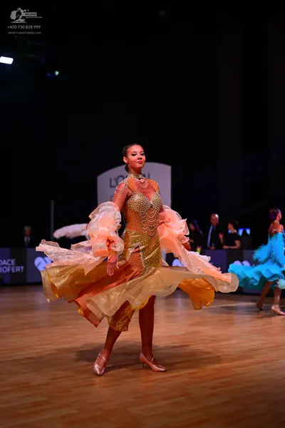 Dancesport competitor: Female dancer 1: gold ballroom dress with a sequined bodice and large, flowing, 